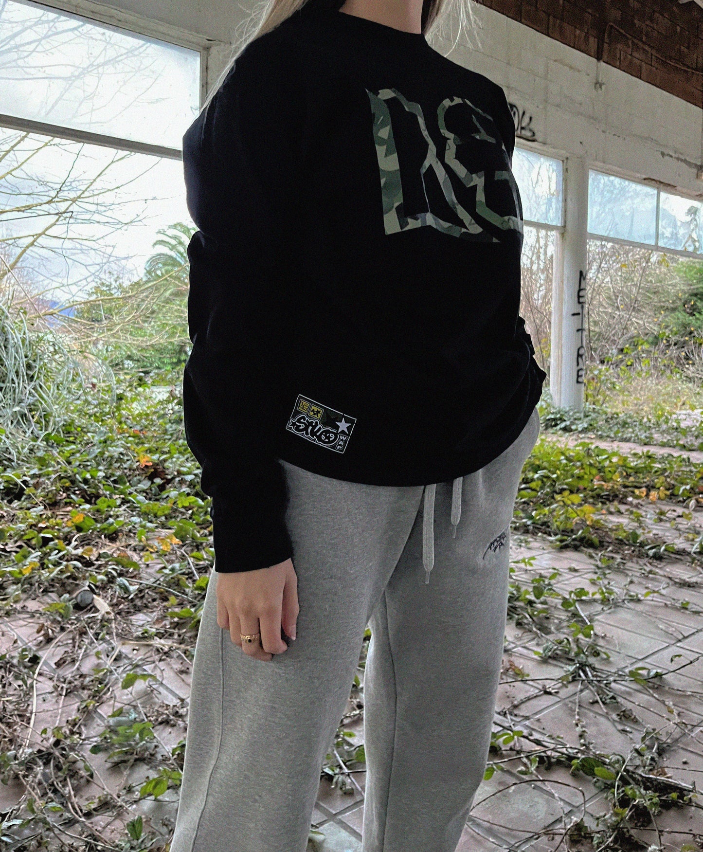 urban girl wearing a long sleeve t-shirt with camouflage accents, behind a wild urban scene