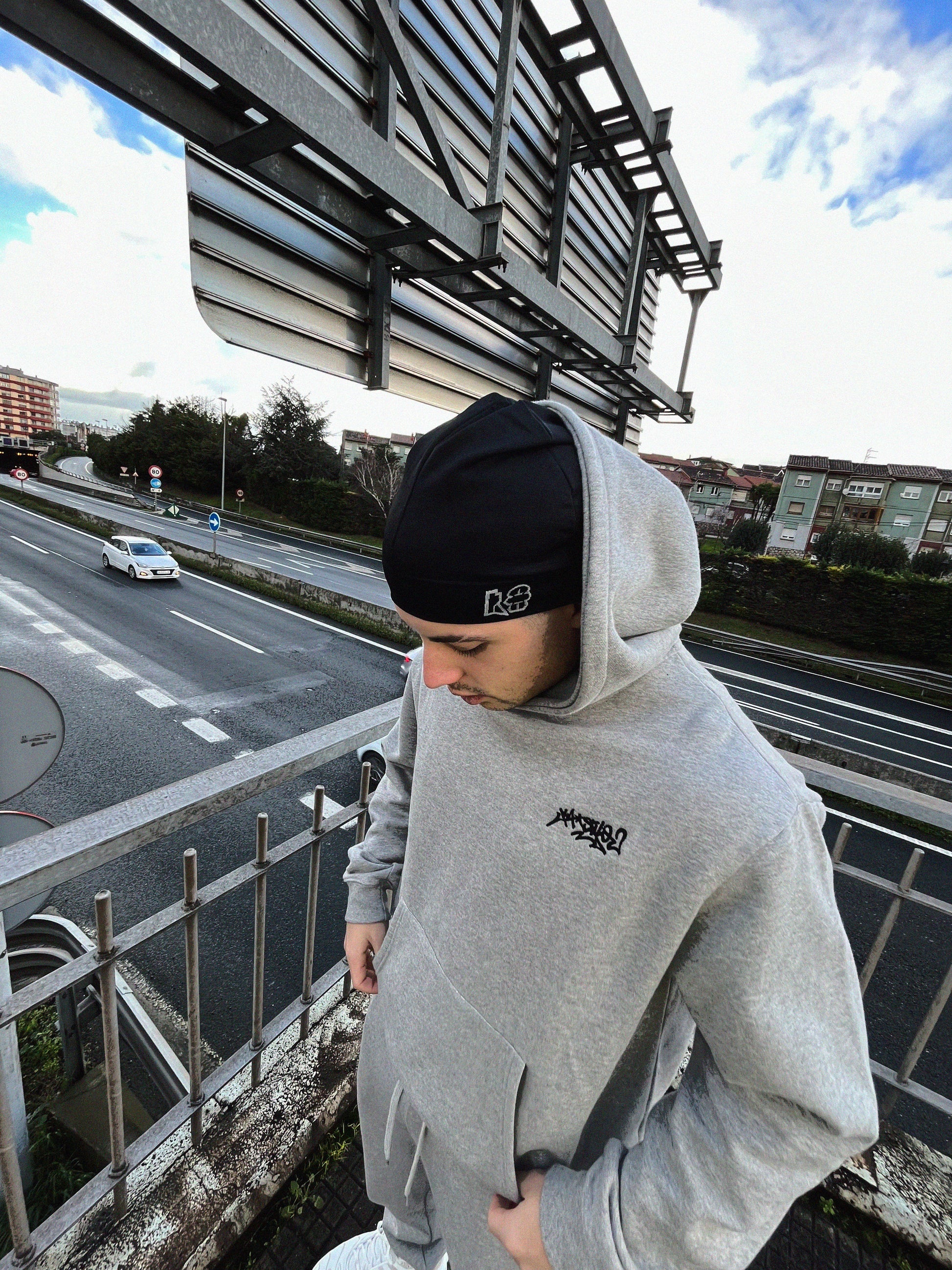 Hip-hop enthusiast rocking a grey streetwear hat and hoodie on the top of a bridge.